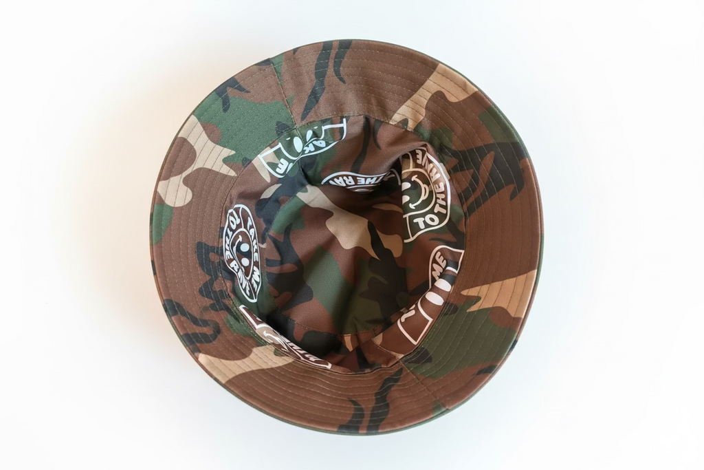 Close-up of the inside of a camouflage bucket hat, showing a brown, green, and tan camo pattern with white printed circular logos around the inner brim.